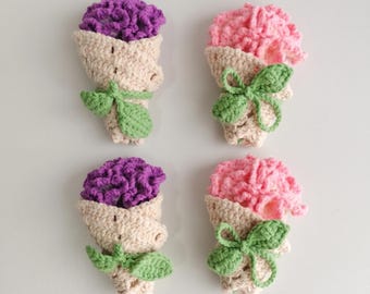 May include: Four crocheted flower bouquets. Two bouquets have purple flowers, and two have pink flowers. Each bouquet is wrapped in a beige cone with green leaves and a bow. The bouquets are arranged on a white background.