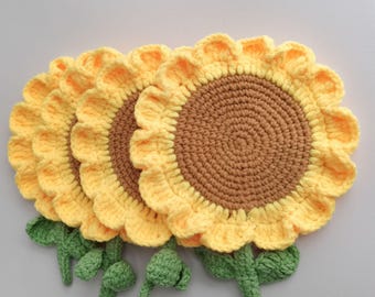 May include: Crocheted sunflower coasters. The coasters are yellow with brown centers, green stems, and leaves. The petals have a scalloped edge. The coasters are handmade and add a touch of nature to any home decor.