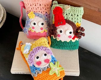 May include: Three handmade crochet pouches featuring whimsical character faces. One pouch is pink with a blue-haired figure, one is green with a brown-haired figure in a red hat, and one is orange with a purple-haired figure and a green starfish accent.