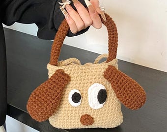 May include: A beige crochet handbag shaped like a dog's face, featuring brown ears and handle, and black and white eyes. The bag has a small, rounded shape, perfect for carrying essentials. The bag is handmade.
