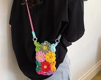 May include: A small crossbody bag crafted from multicolored crocheted flower motifs in shades of pink, yellow, orange, green, and blue. The bag features a long, thin pink cord strap attached with light blue rings and a single white bead closure.