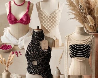 Könnte beinhalten: Eine Kollektion handgefertigter Perlenoberteile und Perlenspitzenkleidung auf Schaufensterpuppen. Die Artikel umfassen pinke, weiße, schwarze und orangefarbene Perlen-BHs, aufwendige schwarze und cremefarbene Spitzenoberteile sowie Perlenketten.