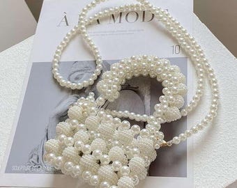 May include: A white beaded handbag with a matching beaded handle and shoulder strap. The bag is square-shaped and features a textured surface made of small, round beads. The strap and handle are made of smaller, strung beads. The bag rests on a magazine with the text "A MOD".