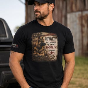 May include: A black t-shirt featuring a graphic of a German Shepherd dog against a distressed American flag background. The text reads: LOYALTY ISN'T OPTIONAL. IT'S WHO LOYALTY IT'S WHO I AM. A paw print icon is below the text. A matching black cap is worn.