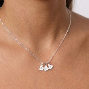 May include: A silver-coloured chain necklace featuring three small heart-shaped charms. Each charm is engraved with a single uppercase letter, spelling out the name DAN, with one letter per heart. The necklace has a delicate link chain design.