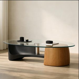 Op de afbeelding: Moderne ovale salontafel met een helder glazen blad. De basis is een combinatie van zwart en natuurlijk hout. Kleine zwarte decoratieve items staan op de tafel. De tafel is ongeveer 122 cm lang.