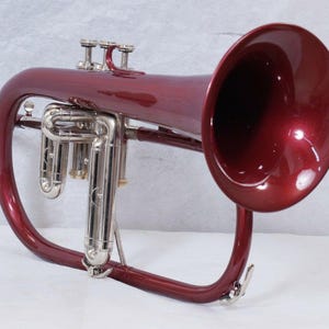 May include: A burgundy flugelhorn with silver-colored valves and trim. The instrument has a shiny finish and a large bell. The flugelhorn is a brass instrument, similar to a trumpet, often used in jazz and other genres.