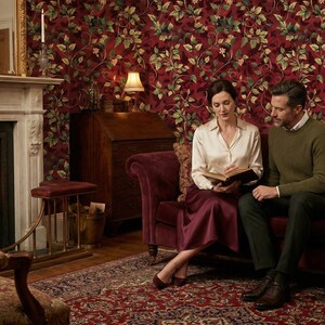 Peut inclure: Int&eacute;rieur chaleureux avec chemin&eacute;e, tapis &agrave; motifs et canap&eacute; bordeaux. Un couple lit un livre sur le canap&eacute;. Les murs sont orn&eacute;s d'un papier peint floral et un bureau en bois est visible. Ambiance cosy et &eacute;l&eacute;gante.