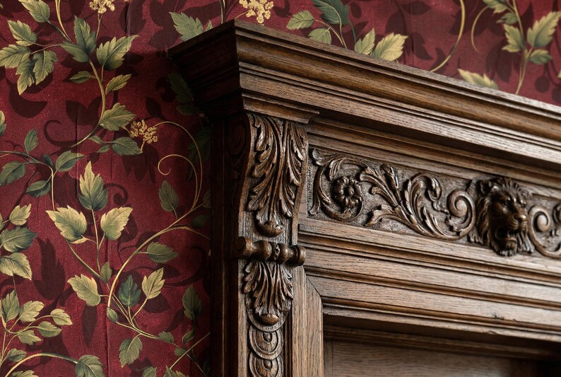 Peut inclure: Gros plan sur une armoire en bois fonc&eacute; avec des sculptures complexes. L'armoire pr&eacute;sente des motifs floraux et des t&ecirc;tes de lion d&eacute;taill&eacute;s. Le fond est un papier peint bordeaux avec des motifs floraux verts et jaunes.