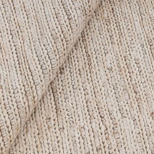 Puede incluir: Primer plano de una alfombra beige tejida con un patrón texturizado y acanalado. La alfombra está hecha de fibras naturales gruesas, con una sección doblada que revela la parte inferior. El color neutro y la textura sugieren un estilo rústico y acogedor.