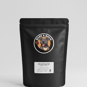 Może przedstawiać: Czarny worek z kawą z logo "Bark & Brew" przedstawiającym uśmiechniętego psa z filiżanką kawy. Na worku znajduje się napis "House Blend" oraz tekst o certyfikacie Fair Trade. Worek jest zapieczętowany.