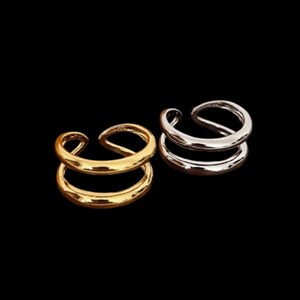May include: Two double-band rings, one gold-toned and one silver-toned, are shown against a black backdrop. The rings have a modern, minimalist design, with a smooth, rounded band. The rings are likely made of metal and are suitable for everyday wear.