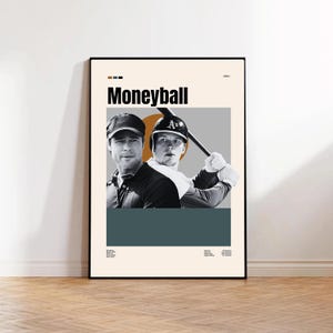 May include: A framed poster featuring the movie title "Moneyball" in bold black letters. The poster includes two grayscale images of men, one wearing a baseball cap. The background has geometric shapes in orange, gray, and teal.