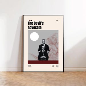 May include: A framed movie poster for "The Devil's Advocate" featuring two men in suits. The poster has a beige background with a gray and red design element. The title is in bold black letters.