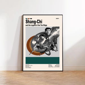 May include: A framed movie poster for "Shang-Chi and the Legend of the Ten Rings" with a beige background. The poster features a central image of the main characters and a dragon, with the title and year displayed at the top. The poster is in a black frame.