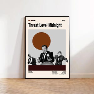May include: A framed poster with the title "Threat Level Midnight" and the year 2005. The poster features three men in suits, a brown circle, and a beige background. The poster is displayed on a wooden floor.