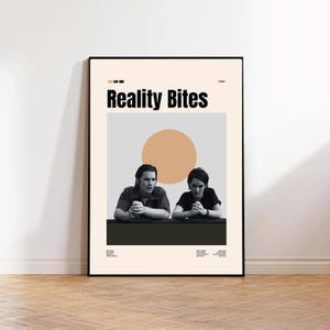 May include: A framed poster featuring the movie title "Reality Bites" in bold black letters. The poster has a beige background with a peach-colored circle and two people. The poster is displayed on a wooden floor.