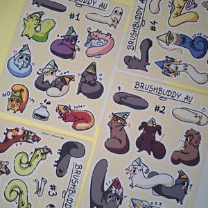 May include: Three sticker sheets labeled BRUSHBUDDY AU #1, #2, #3, and #4 featuring various cartoon creatures in party hats. The colorful illustrations depict small, whimsical characters in different poses, some sleeping, some smiling, and some with text like hehe.