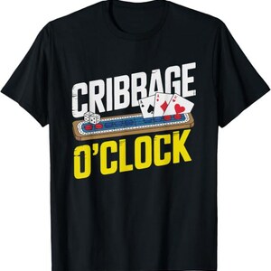 Può includere: Una t-shirt nera con la grafica di una tavola da cribbage in legno con pedine rosse e blu, due dadi bianchi e tre carte da gioco. Il testo riporta "CRIBBAGE" in lettere bianche sopra la tavola e "O'CLOCK" in lettere gialle al di sotto.