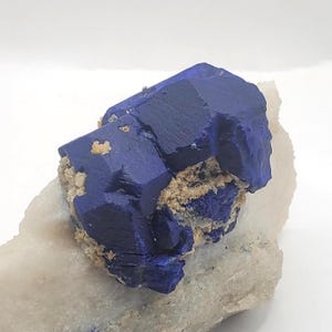 May include: A striking, deep blue azurite crystal formation with a complex, angular structure. The azurite is set against a backdrop of beige and white minerals, creating a beautiful contrast. This natural specimen is a unique piece for collectors.