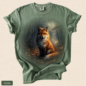 May include: A moss green t-shirt with a detailed illustration of a fox in a forest. The fox has orange and white fur, set against a forest backdrop. The shirt has rolled-up sleeves.