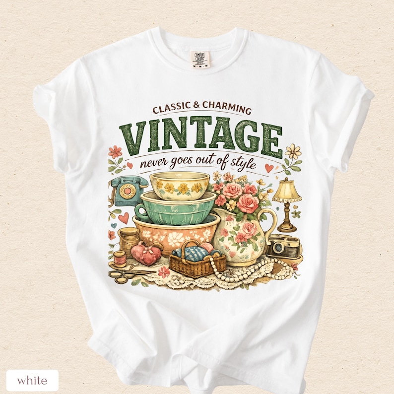May include: A white t-shirt featuring a graphic print with the text "CLASSIC & CHARMING VINTAGE never goes out of style". The illustration includes stacked bowls, a floral pitcher, a rotary phone, a lamp, a camera, and sewing supplies.
