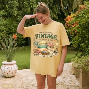 May include: A butter yellow t-shirt featuring a graphic print with the text CLASSIC & CHARMING VINTAGE never goes out of style. The illustration includes stacked bowls, a floral pitcher, a rotary phone, a lamp, and sewing supplies.