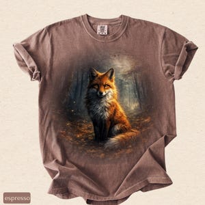 May include: Espresso-coloured t-shirt with a detailed illustration of a fox in a forest. The fox has orange and white fur, set against a backdrop of trees and foliage. The shirt has a crew neck and short sleeves.