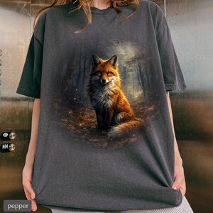 May include: Charcoal grey t-shirt with a detailed illustration of a fox in a forest. The fox has orange and white fur, set against a forest backdrop. The shirt has a relaxed fit.