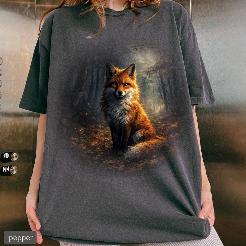 May include: Charcoal grey t-shirt with a detailed illustration of a fox in a forest. The fox has orange and white fur, set against a forest backdrop. The shirt has a relaxed fit.