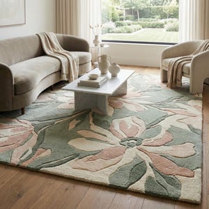 May include: A floral patterned rug in a living room setting. The rug features large flowers in shades of green, pink, and cream. The room also includes a sofa, chairs, and a marble coffee table. The rug is a prominent feature.