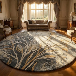 May include: A large, round area rug with a tree branch design. The rug features a dark gray background with beige and gold-colored branches. The rug is placed in a room with a sofa, chairs, and a large window.