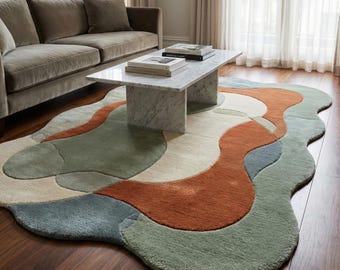 May include: An abstract area rug with a wavy, organic design. The rug features a combination of colors, including rust, sage green, cream, and blue. The rug is placed on a hardwood floor, with a marble coffee table and a sofa in the background.