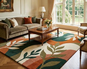 May include: A colorful area rug with a botanical design in a living room setting. The rug features a pattern of stylized leaves in shades of green, orange, and cream. The room includes a brown sofa, coffee table, and a large arched window.