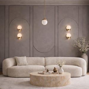 May include: A modern living room with a beige boucle sofa, a round stone coffee table, and a gray rug. The wall is a muted gray with decorative paneling and gold sconces. A pendant light hangs above the coffee table.