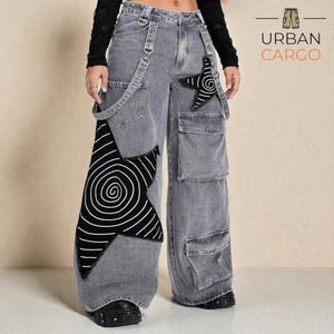 Puede incluir: Pantalones cargo vaqueros grises con parches en forma de estrella con diseños de espirales en blanco y negro. Los pantalones tienen múltiples bolsillos, tirantes y el logo "URBAN CARGO".