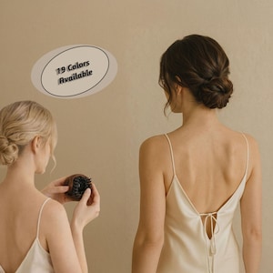 May include: Two women with their backs to the camera, wearing white spaghetti strap tops, with their hair styled in buns. One woman holds a dark brown hairbrush. The image includes text that says "19 Colors Available".