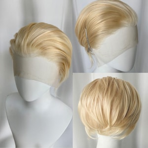 Op de afbeelding: Een blonde pruik met een korte, gelaagde stijl wordt getoond op een mannequinhoofd. De pruik heeft een natuurlijk ogende haarlijn en is gestyled met een zijscheiding. Het haar heeft een lichte, goudblonde kleur.