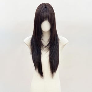 Op de afbeelding: Een lange, gelaagde pruik met donkerbruin haar en een rechte pony. De pruik wordt getoond op een mannequinhoofd tegen een effen witte achtergrond. Het haar heeft een natuurlijke uitstraling met subtiele highlights.