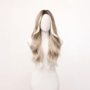 May include: A long, wavy wig with dark brown roots that blend into a light blonde. The wig is displayed on a white mannequin head and shoulders against a white backdrop. The hair has a natural wave.