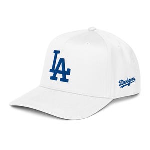 Könnte beinhalten: Weiße Baseballkappe mit dem blauen "LA"-Logo auf der Vorderseite und dem Wort "Dodgers" in blauer Schrift auf der Seite. Die Kappe hat einen gebogenen Schirm und eine strukturierte Passform, geeignet für Sport oder Freizeit.