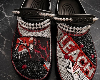 May include: A pair of black clogs decorated with silver spikes on the heel straps. The shoes are covered in red, white, and black rhinestones. One shoe features an anime character illustration, while the other displays the word BLEACH in crystals.