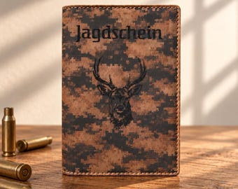 May include: A rectangular leather wallet featuring a brown and black digital camouflage pattern. The front displays a black graphic of a deer head and the text Jagdschein in a dark font. The edges are stitched with matching brown thread.