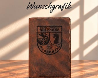 May include: A brown leather passport holder featuring a dark engraved crest with the text Schützenverein Sulzdorf Hessental. The cover displays a shield design with a lion, an eagle, a unicorn, and a target symbol. The text Wunschgrafik is visible.