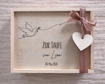 May include: A wooden box with a dove illustration and the text "ZUR TAUFE von Leon 03. Mai 2026". The box is tied with a mauve ribbon and a wooden heart-shaped tag.