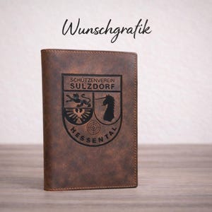 Könnte beinhalten: Ein braunes Lederportemonnaie mit einem schwarzen Emblem mit einem Löwen, einem Einhorn und dem Text "SCHÜTZENVEREIN SULZDORF HESSENTAL". Der Text "Wunschgrafik" ist oben in Kursivschrift geschrieben.