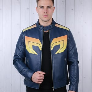 Puede incluir: Chaqueta de cuero azul marino con diseños geométricos amarillos y naranjas en el pecho y los hombros. La chaqueta tiene cuello alzado, cremallera frontal y bolsillos laterales. Una prenda de abrigo elegante.