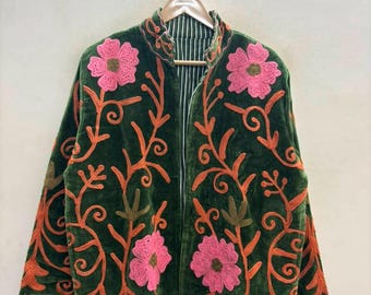 May include: A dark green velvet jacket featuring vibrant pink embroidered flowers and orange swirling vine patterns. The jacket has a high collar, long sleeves, and a front opening that reveals a white and dark green striped lining on the interior.
