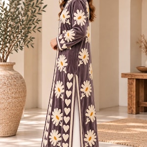 May include: A long-sleeved, calf-length grey velvet coat featuring a cream-coloured floral and heart-shaped pattern. The garment has a high collar, side slits, and is worn over plain white trousers. The Khushi Craft House logo is visible.