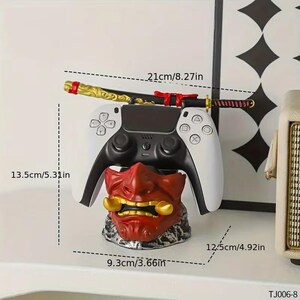 K&ouml;nnte beinhalten: Ein wei&szlig;-schwarzer Videospiel-Controller auf einem roten Oni-Masken-St&auml;nder. Ein Miniatur-Katana-Schwert, 21 cm lang, liegt auf dem Controller. Der St&auml;nder ist 9,3 cm breit und 12,5 cm hoch.
